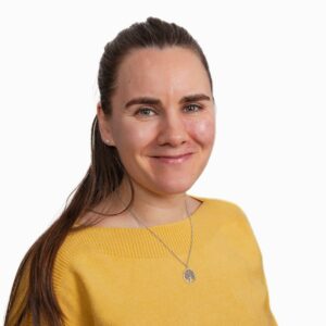 Hymyilevä ruskeatukkainen naishenkilö keltaisessa paidassa